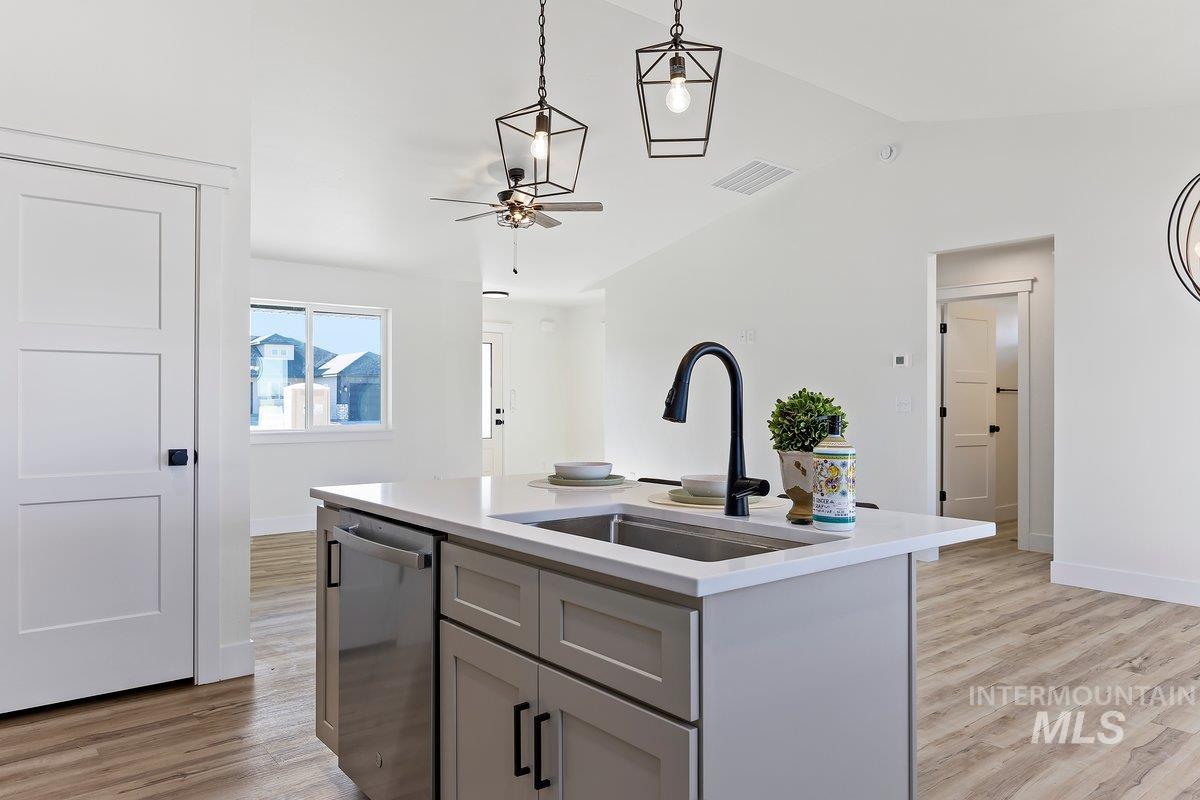 Kitchen with decorative light fixtures, light wood-type flooring, stainless steel dishwasher, gray cabinetry, and lofted ceiling