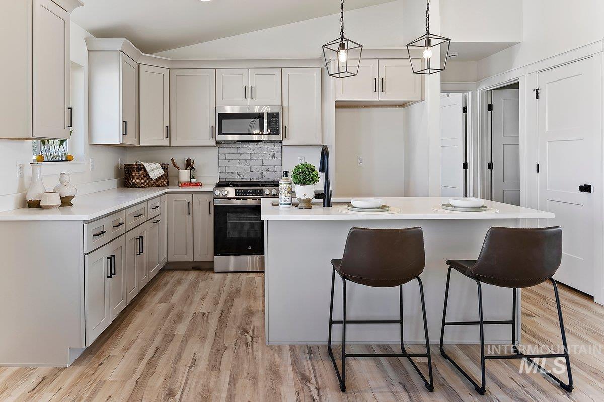 Kitchen with a breakfast bar area, appliances with stainless steel finishes, decorative light fixtures, a center island, and light wood-style floors