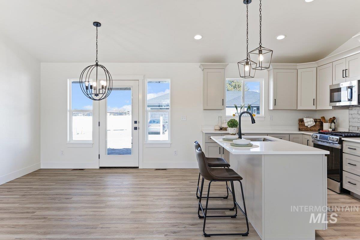 Kitchen with a chandelier, stainless steel appliances, hanging light fixtures, a center island with sink, and recessed lighting