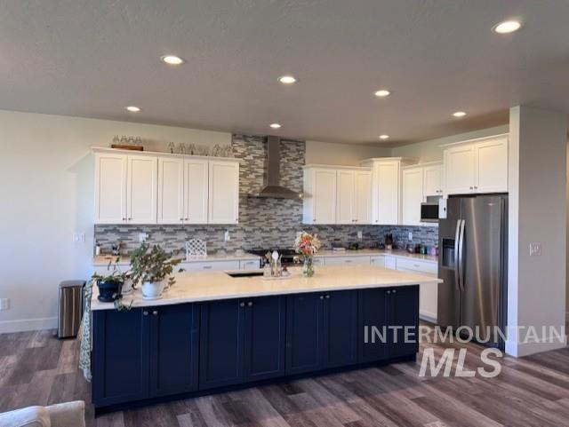 Kitchen featuring white cabinets, stainless steel fridge, backsplash, wall chimney exhaust hood, and recessed lighting