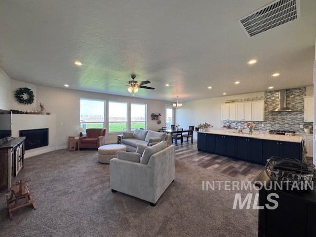 Living room featuring a fireplace, dark colored carpet, a chandelier, recessed lighting, and ceiling fan