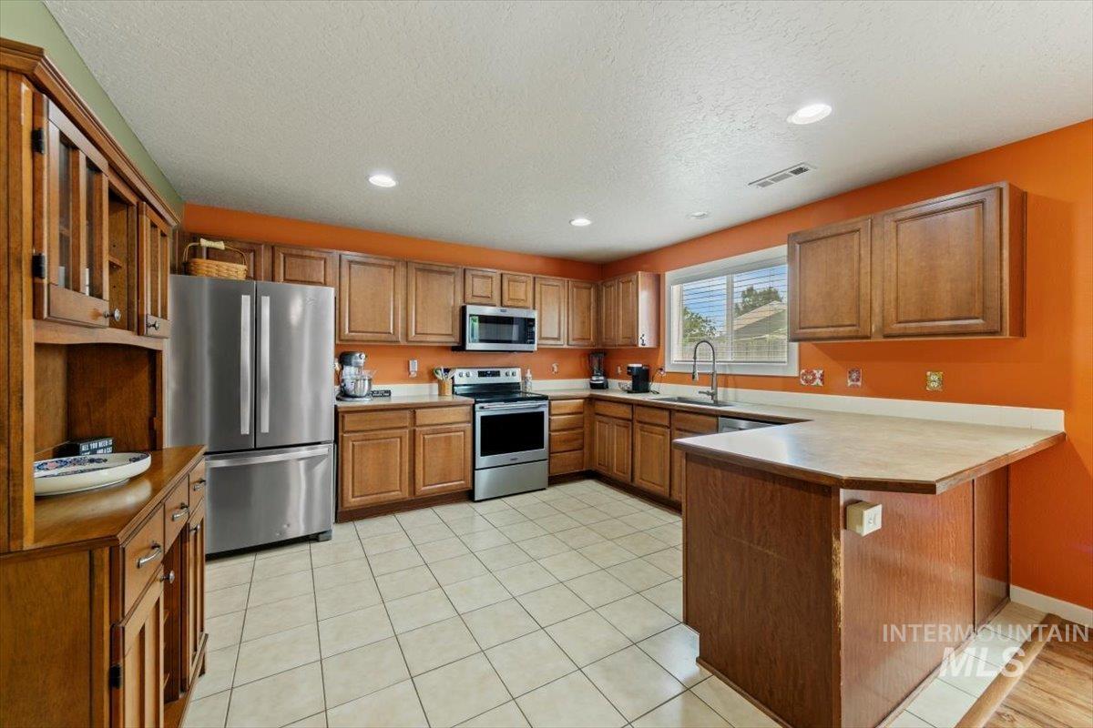 Kitchen featuring appliances with stainless steel finishes, brown cabinetry, recessed lighting, a peninsula, and light tile patterned floors