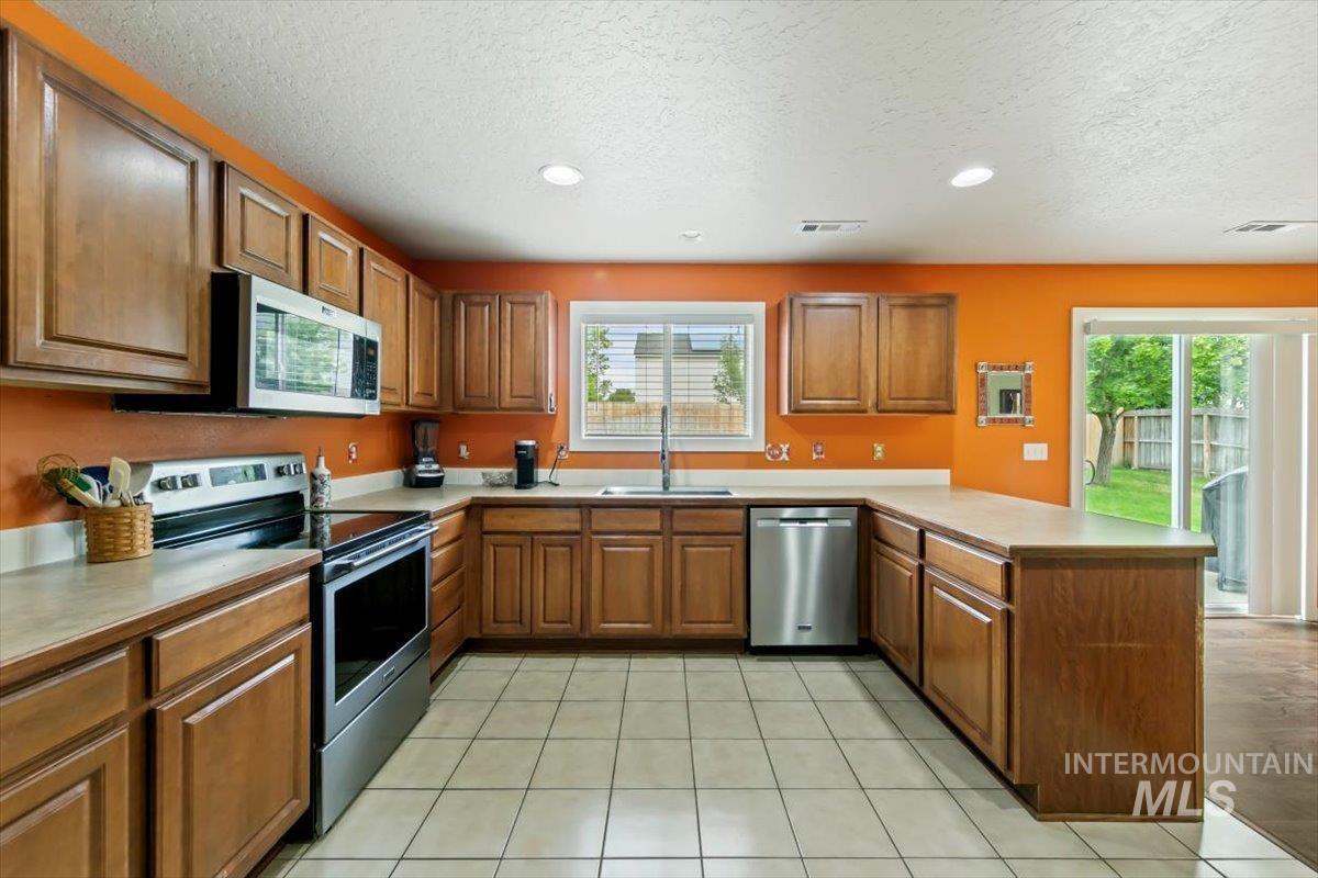Kitchen featuring a peninsula, appliances with stainless steel finishes, brown cabinetry, a textured ceiling, and light countertops