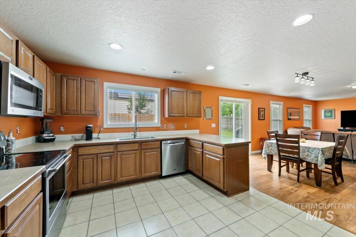 Kitchen featuring appliances with stainless steel finishes, a textured ceiling, light tile patterned flooring, a peninsula, and brown cabinetry