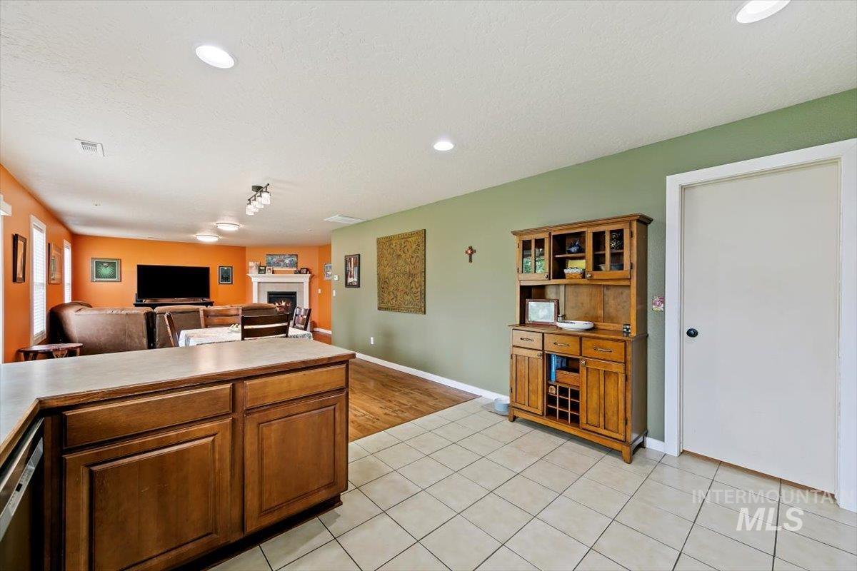 Kitchen with light tile patterned floors, open floor plan, brown cabinets, a warm lit fireplace, and recessed lighting