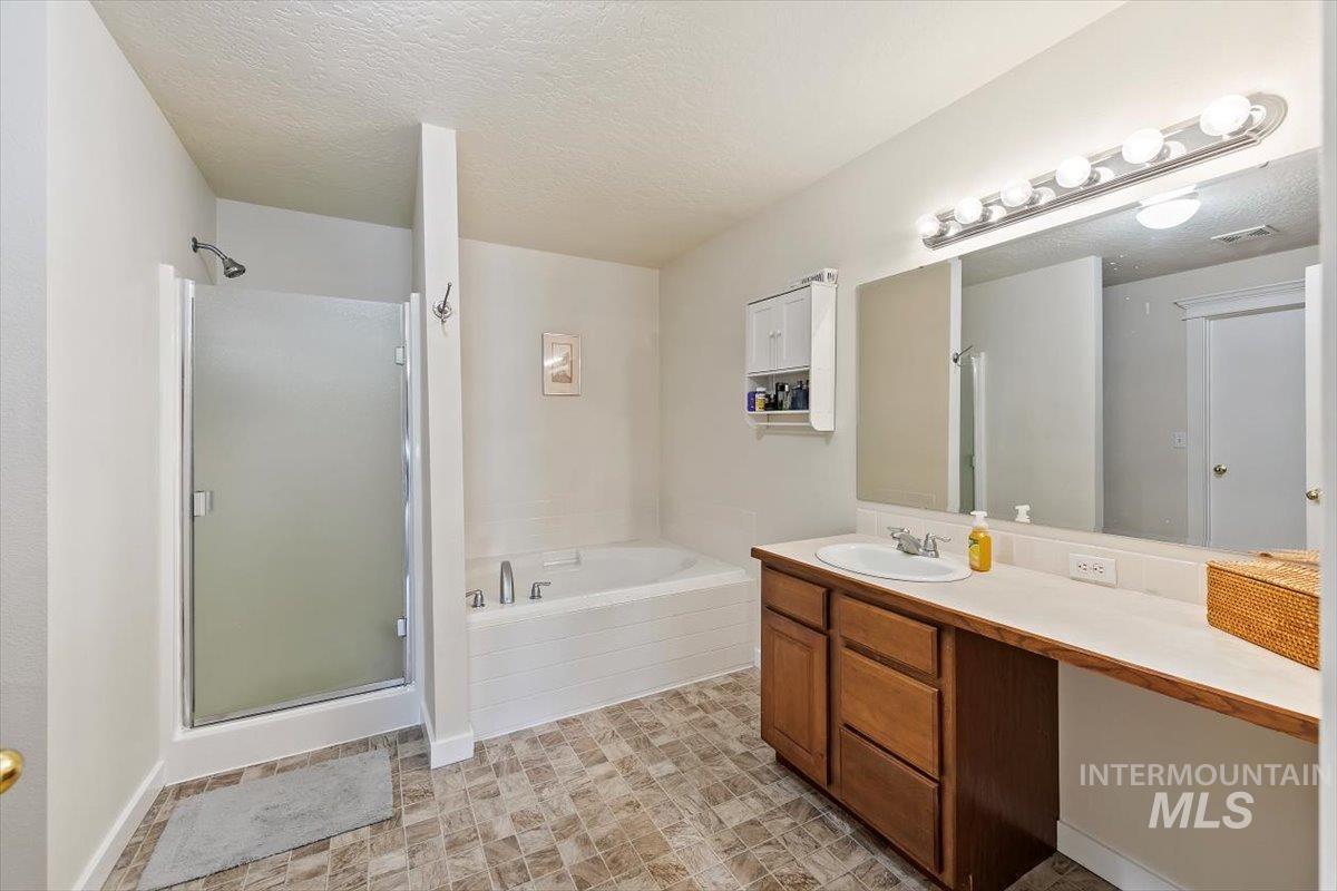 Bathroom with a shower stall, a garden tub, vanity, and a textured ceiling