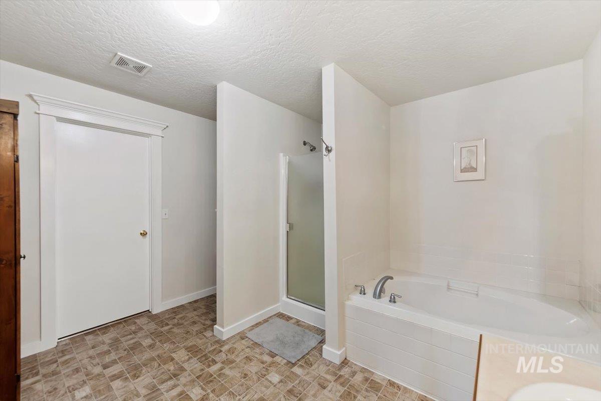 Bathroom featuring a bath, a textured ceiling, and a shower stall