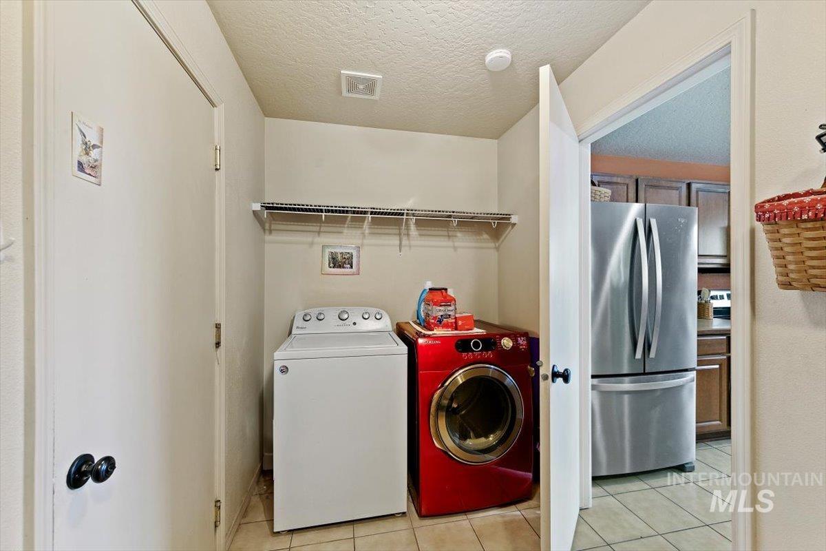 Washroom featuring light tile patterned floors, a textured ceiling, and washing machine and dryer