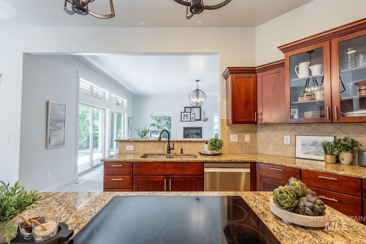 Kitchen with a chandelier, backsplash, black electric stovetop, glass insert cabinets, and light stone counters