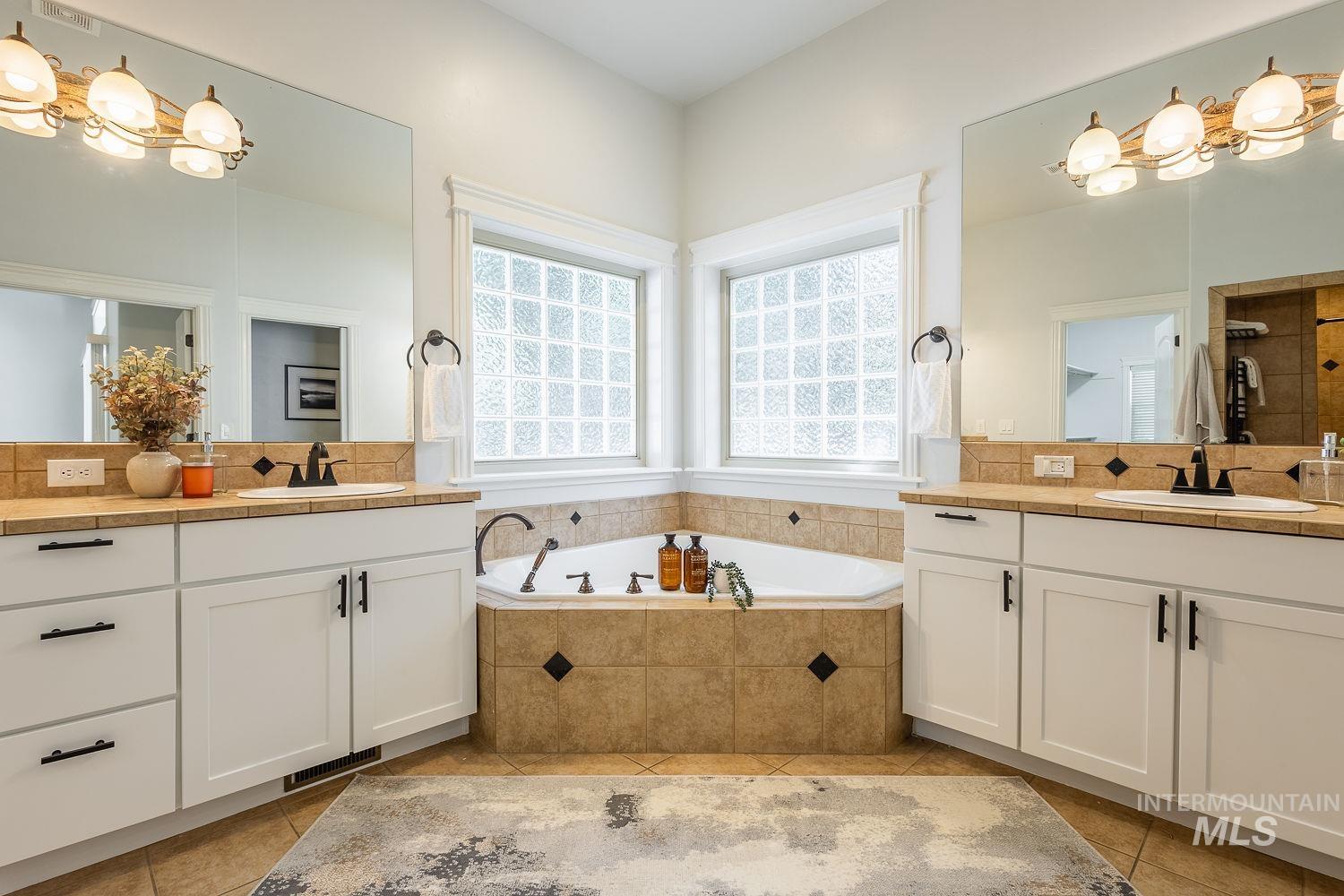 Full bath with two vanities, a bath, light tile patterned floors, and tiled shower