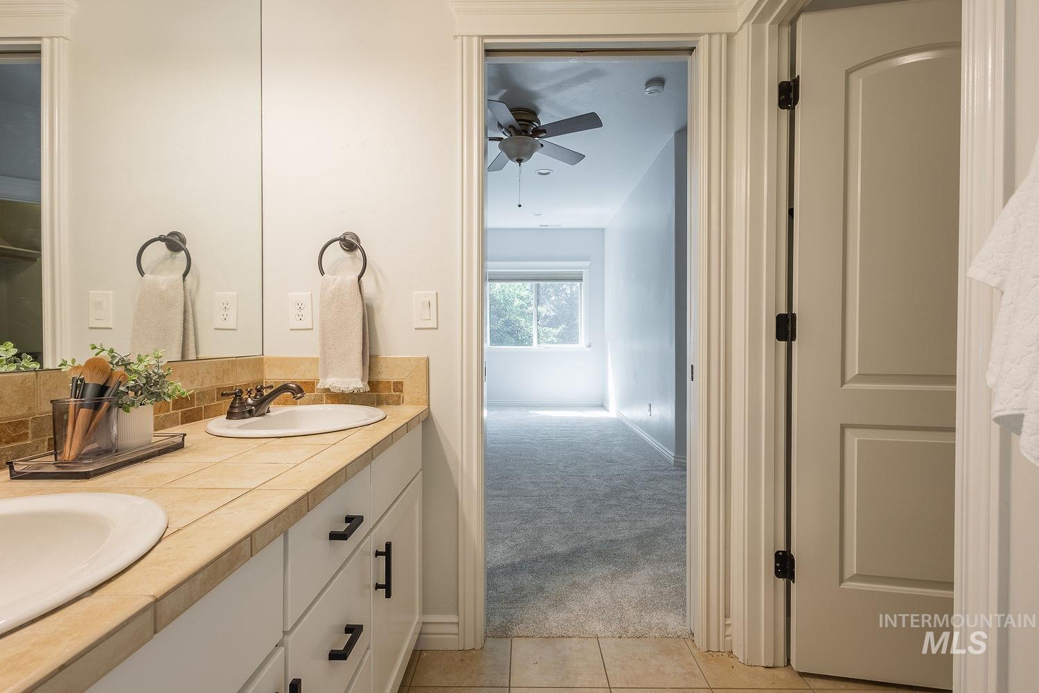 Full bathroom with double vanity, light tile patterned floors, backsplash, and a ceiling fan