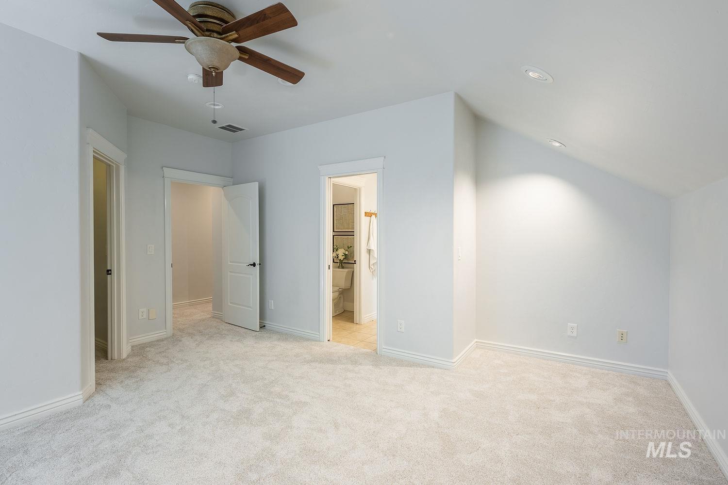 Unfurnished bedroom featuring light carpet, lofted ceiling, ceiling fan, ensuite bathroom, and recessed lighting