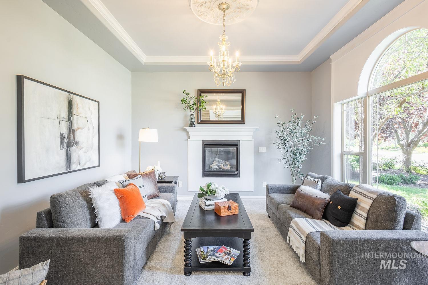 Living room with a glass covered fireplace, a tray ceiling, carpet flooring, a chandelier, and crown molding