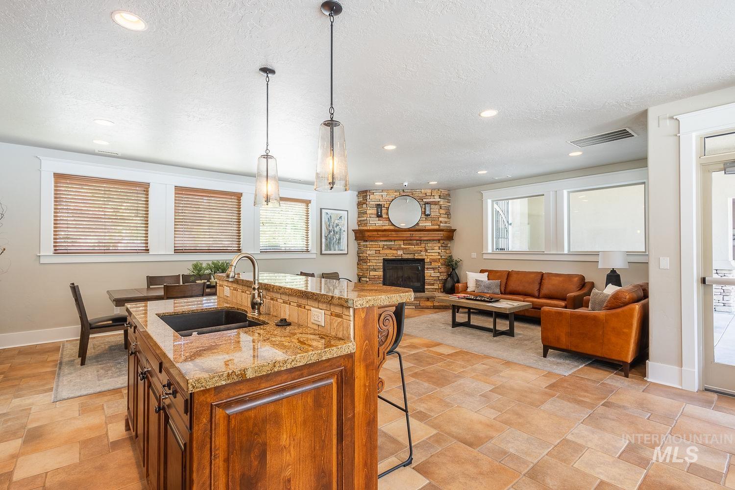 Kitchen featuring a kitchen bar, pendant lighting, light stone counters, brown cabinetry, and an island with sink