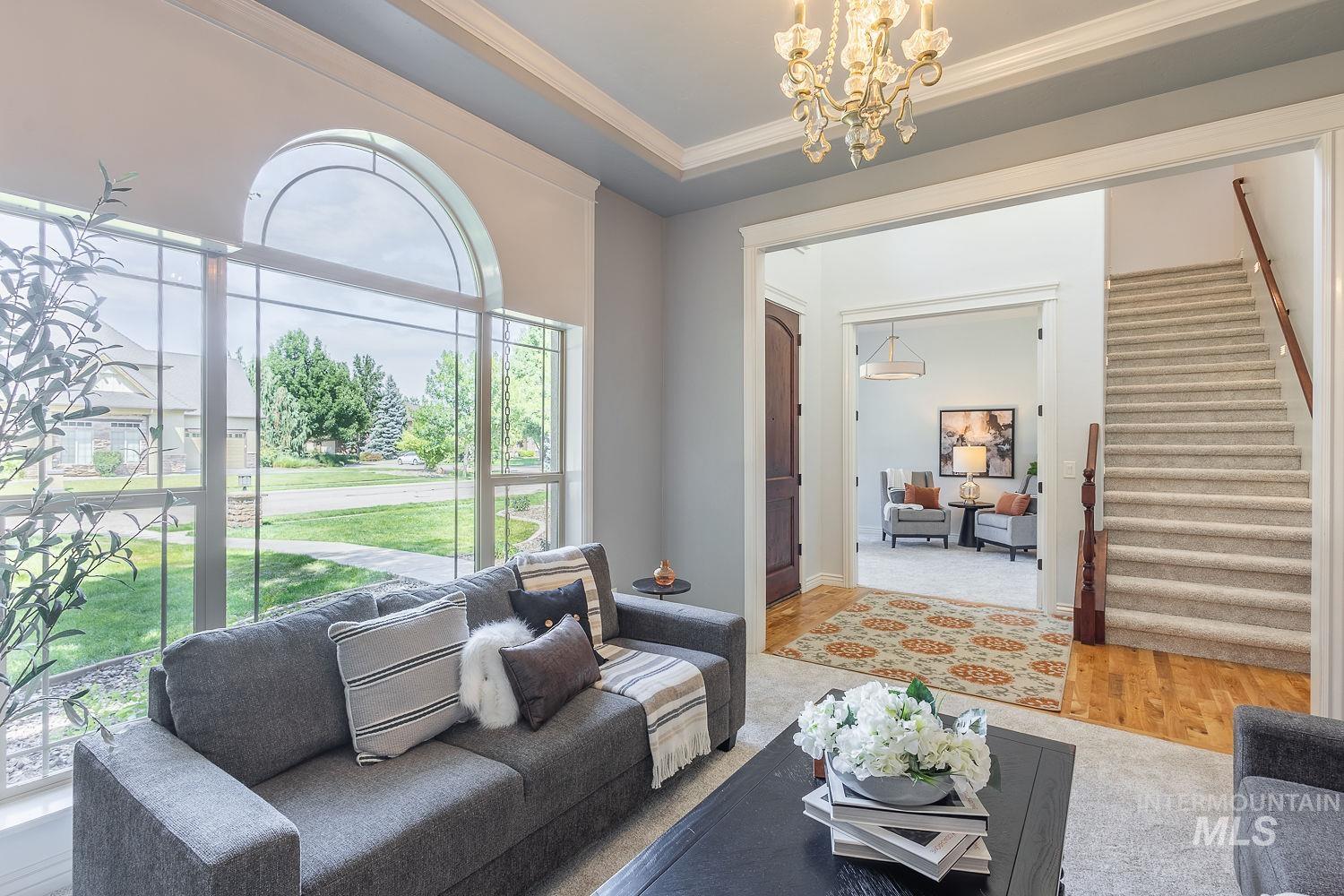 Living room featuring wood finished floors, stairs, ornamental molding, a chandelier, and a raised ceiling