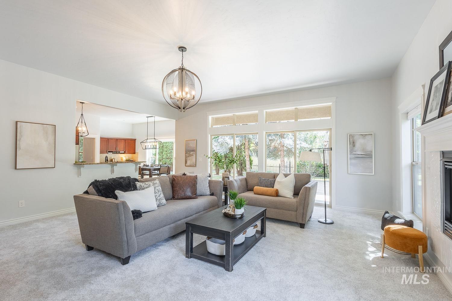 Living area featuring healthy amount of natural light, light carpet, a glass covered fireplace, and a chandelier