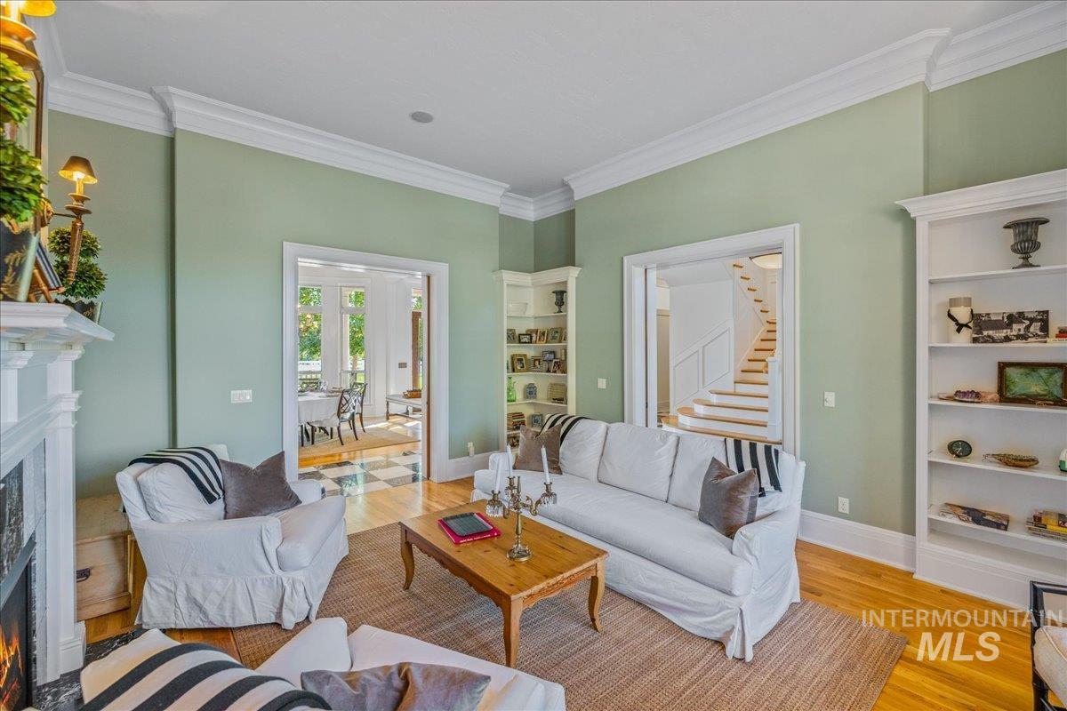 Living area featuring a lit fireplace, ornamental molding, wood finished floors, and stairway