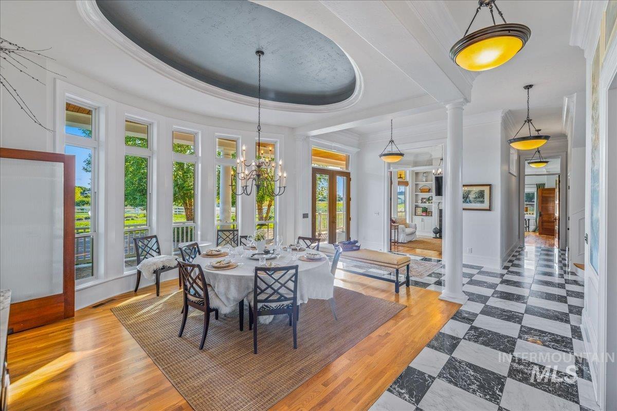 Dining room featuring a tray ceiling, ornate columns, wood finished floors, a chandelier, and crown molding