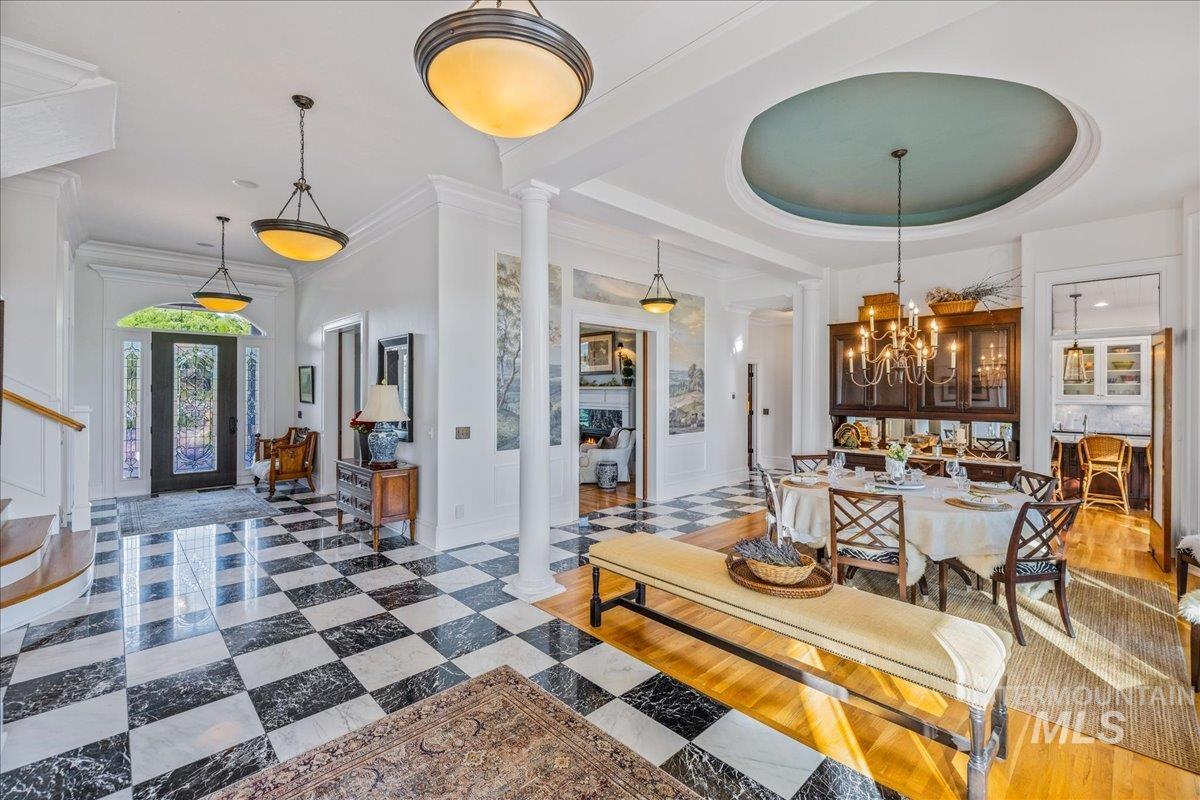 Dining room with stairs, ornate columns, a raised ceiling, a chandelier, and a decorative wall