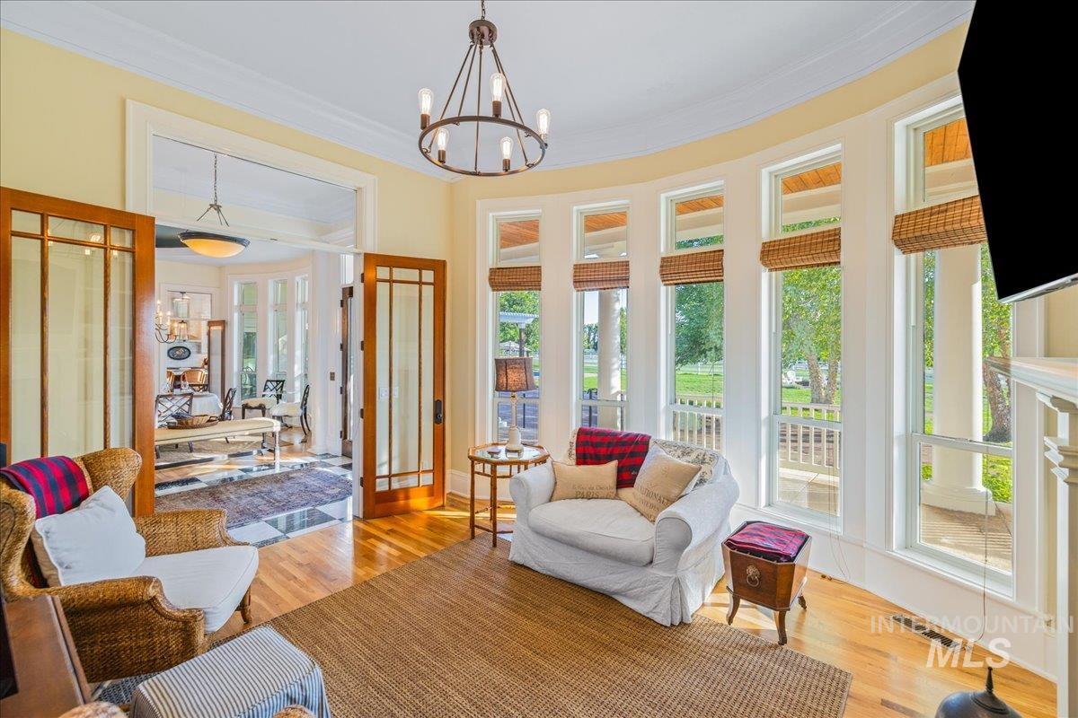 Sunroom / solarium featuring wood finished floors, ornamental molding, and a chandelier