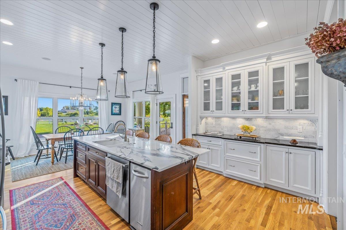 Kitchen with a kitchen breakfast bar, white cabinets, decorative backsplash, hanging light fixtures, and glass insert cabinets