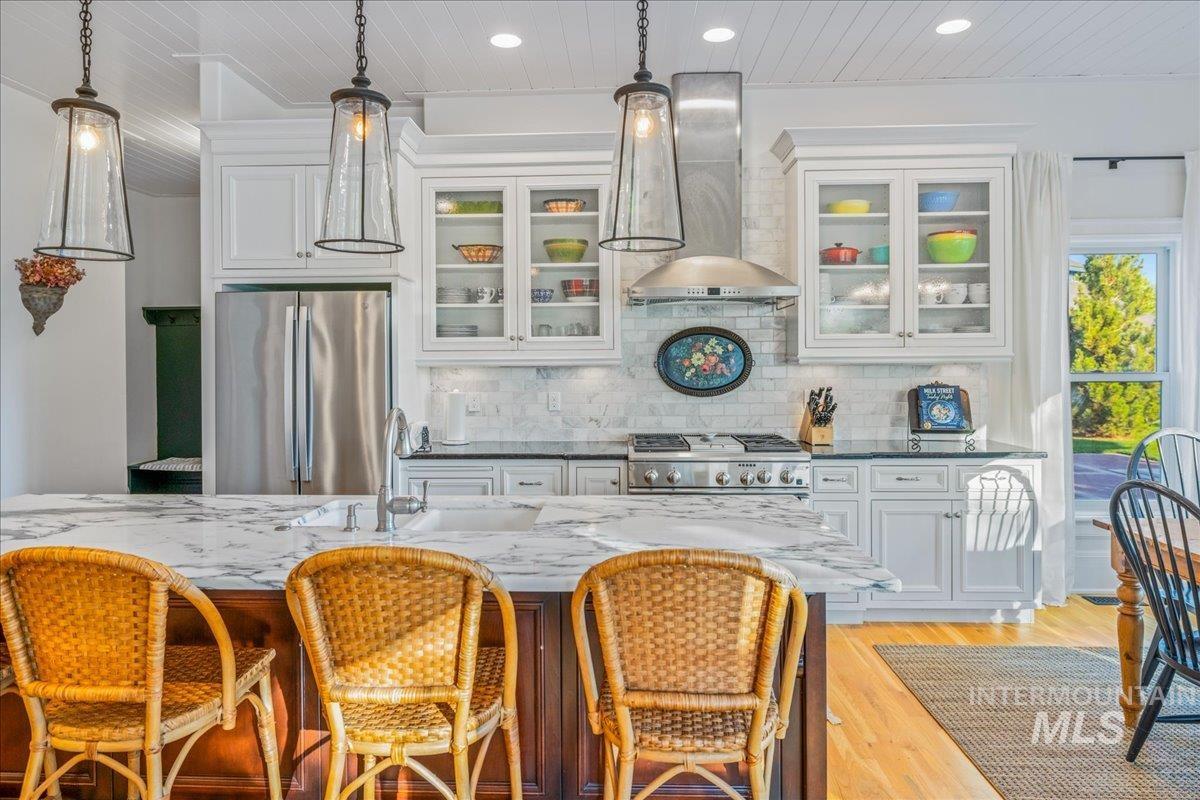 Kitchen featuring glass insert cabinets, white cabinetry, freestanding refrigerator, decorative backsplash, and dark stone counters