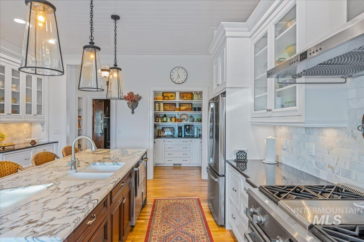 Kitchen featuring glass insert cabinets, tasteful backsplash, white cabinets, and wall chimney exhaust hood