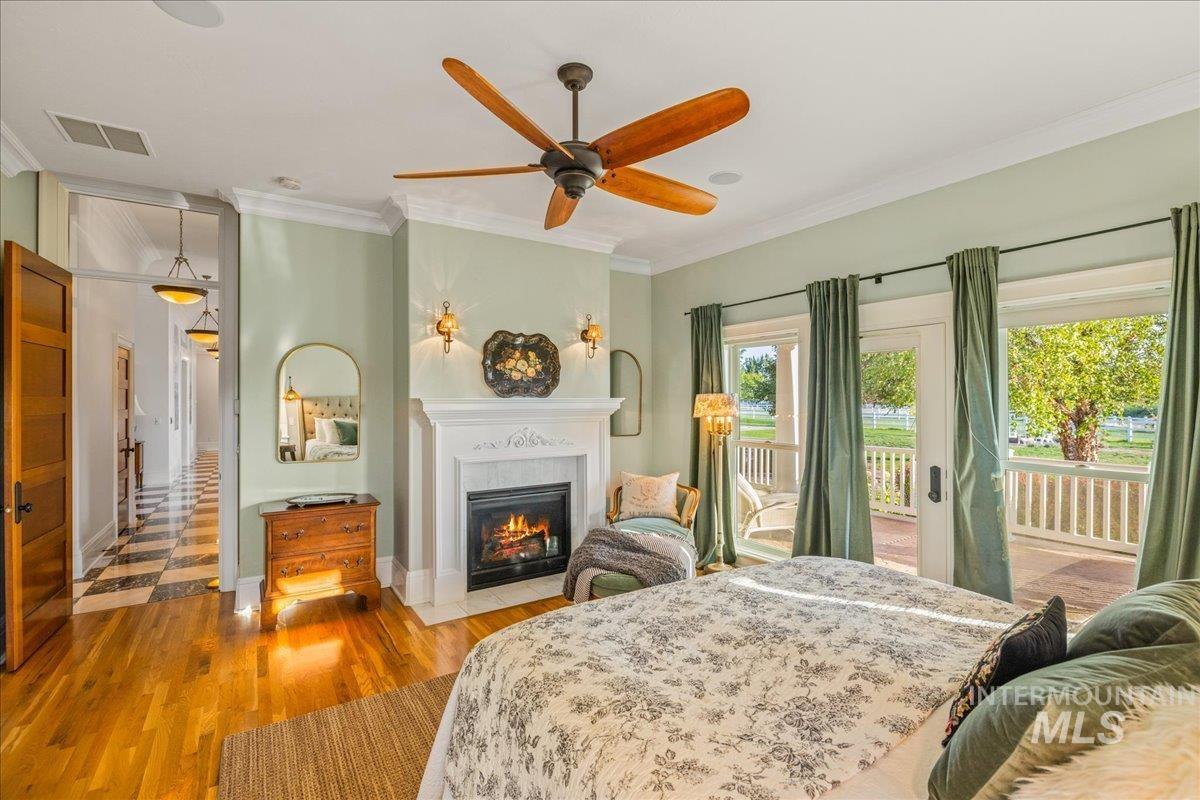 Bedroom with crown molding, wood finished floors, a warm lit fireplace, access to exterior, and a ceiling fan