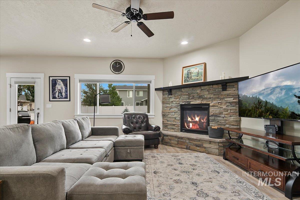 Living area featuring a textured ceiling, light wood-type flooring, a fireplace, ceiling fan, and recessed lighting
