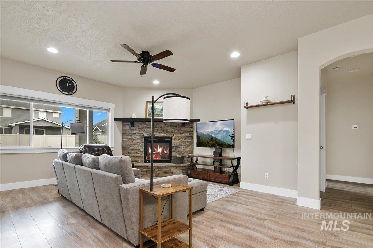 Living area featuring a fireplace, light wood-style floors, ceiling fan, arched walkways, and recessed lighting