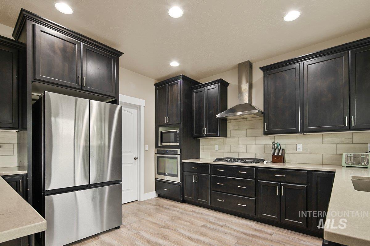 Kitchen with stainless steel appliances, backsplash, wall chimney exhaust hood, light wood-style floors, and recessed lighting