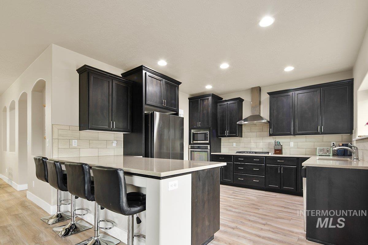 Kitchen with a peninsula, a breakfast bar area, dark cabinetry, backsplash, and recessed lighting