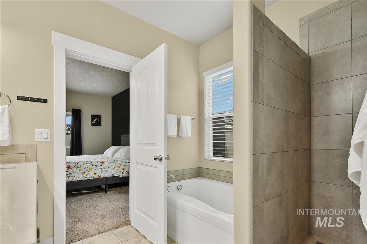 Ensuite bathroom featuring a garden tub and light tile patterned flooring