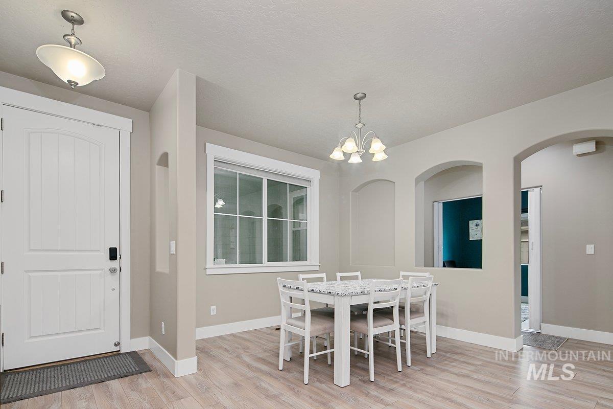 Dining space with a chandelier, arched walkways, light wood finished floors, and a textured ceiling