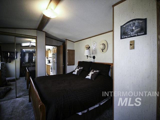 Carpeted bedroom featuring lofted ceiling, a closet, crown molding, and freestanding refrigerator