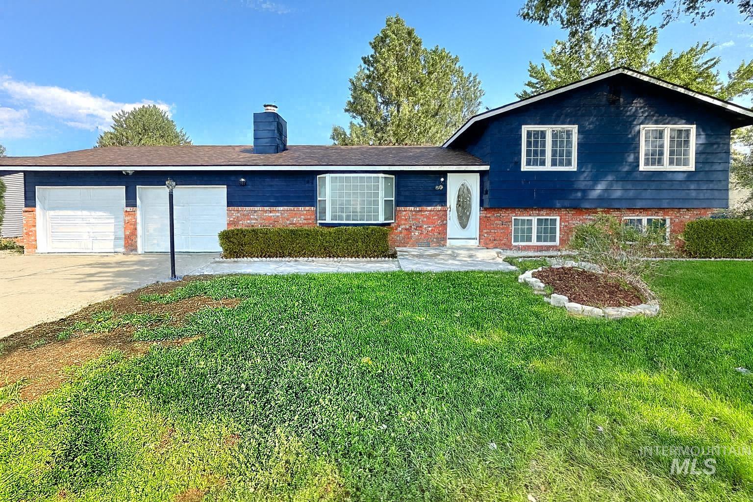 Tri-level home with a chimney, driveway, brick siding, a garage, and a front yard