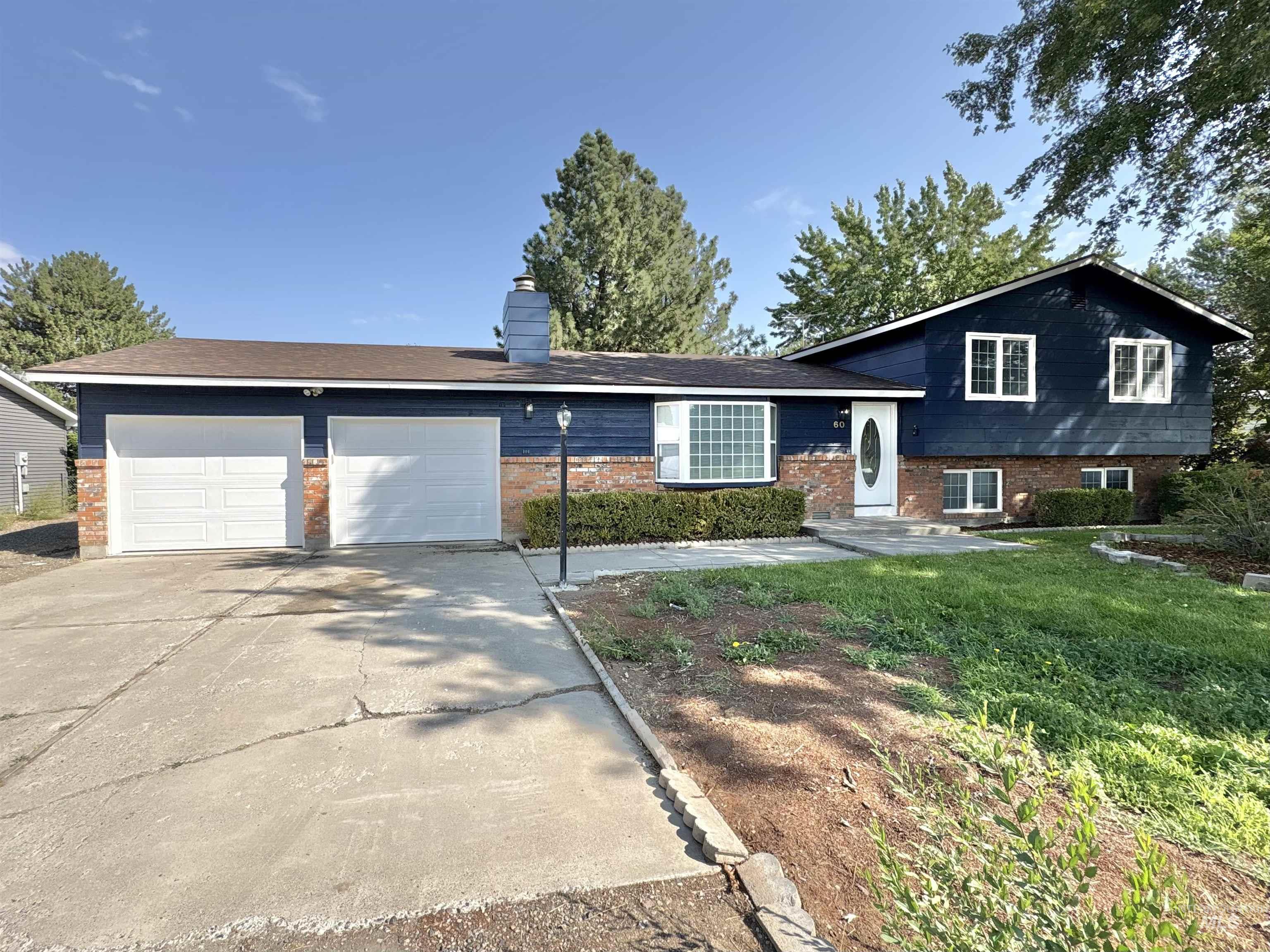Tri-level home with brick siding, concrete driveway, a garage, and a chimney