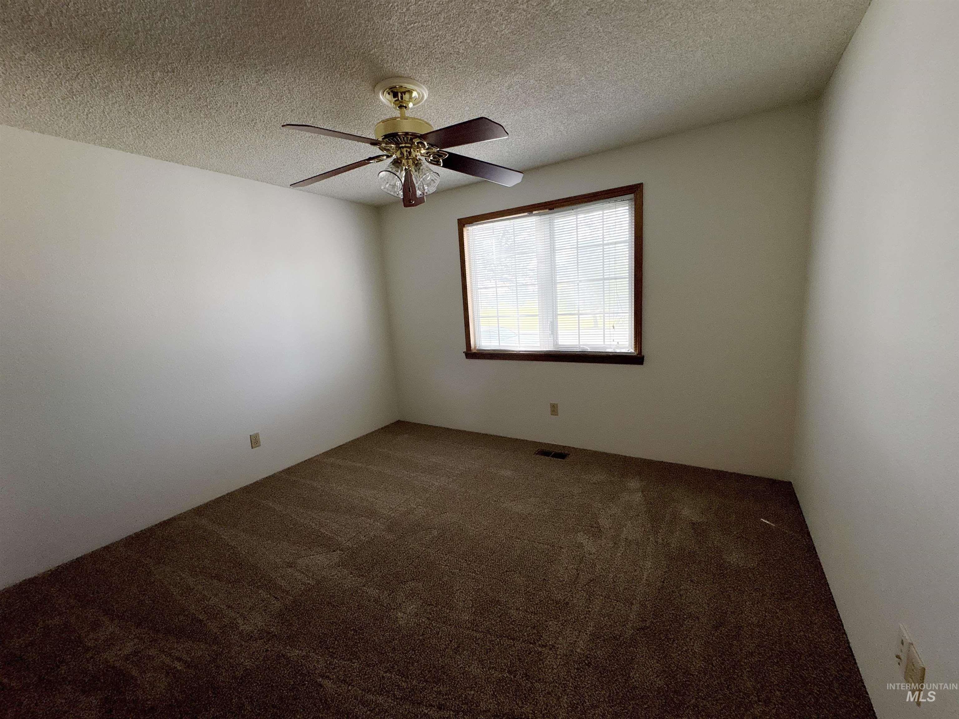 Carpeted empty room with a textured ceiling and a ceiling fan