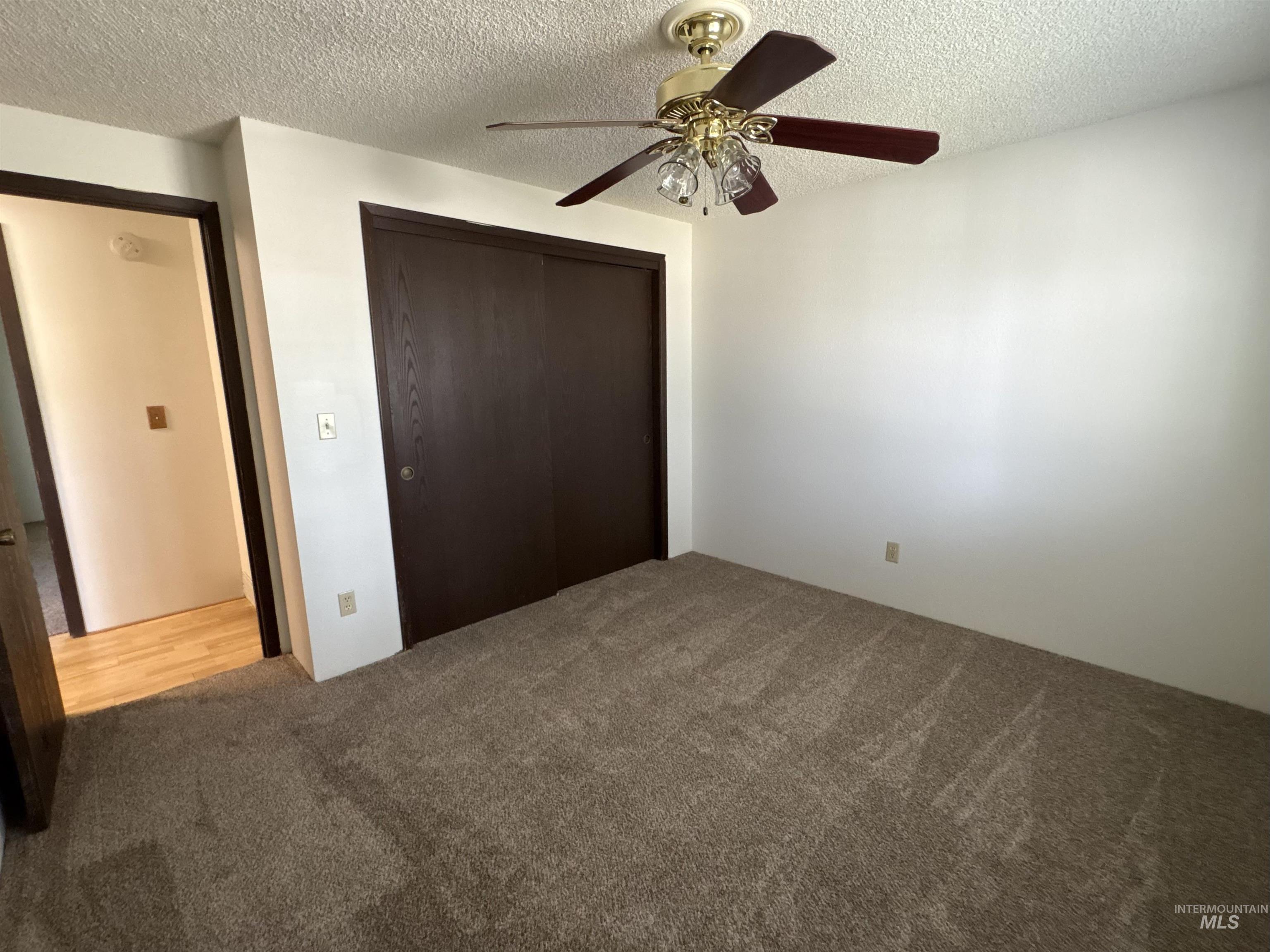 Unfurnished bedroom featuring a closet, a textured ceiling, carpet flooring, and ceiling fan