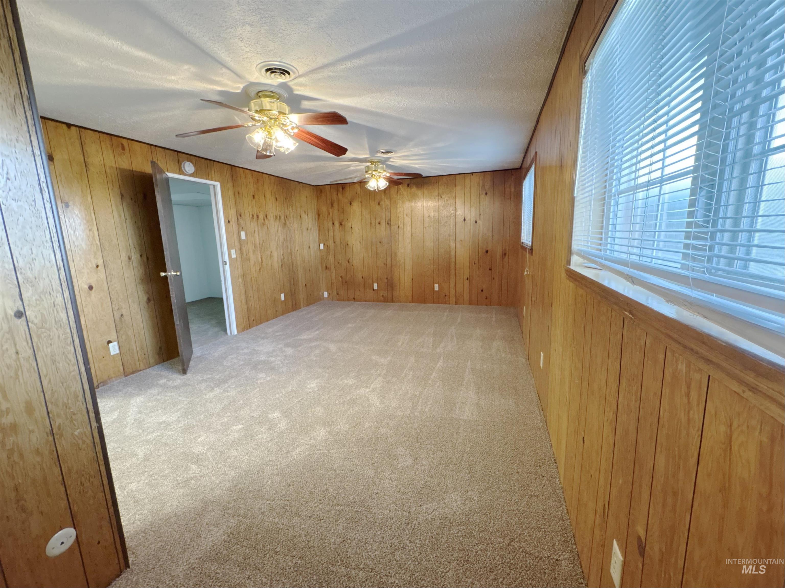 Carpeted empty room with wooden walls and a ceiling fan