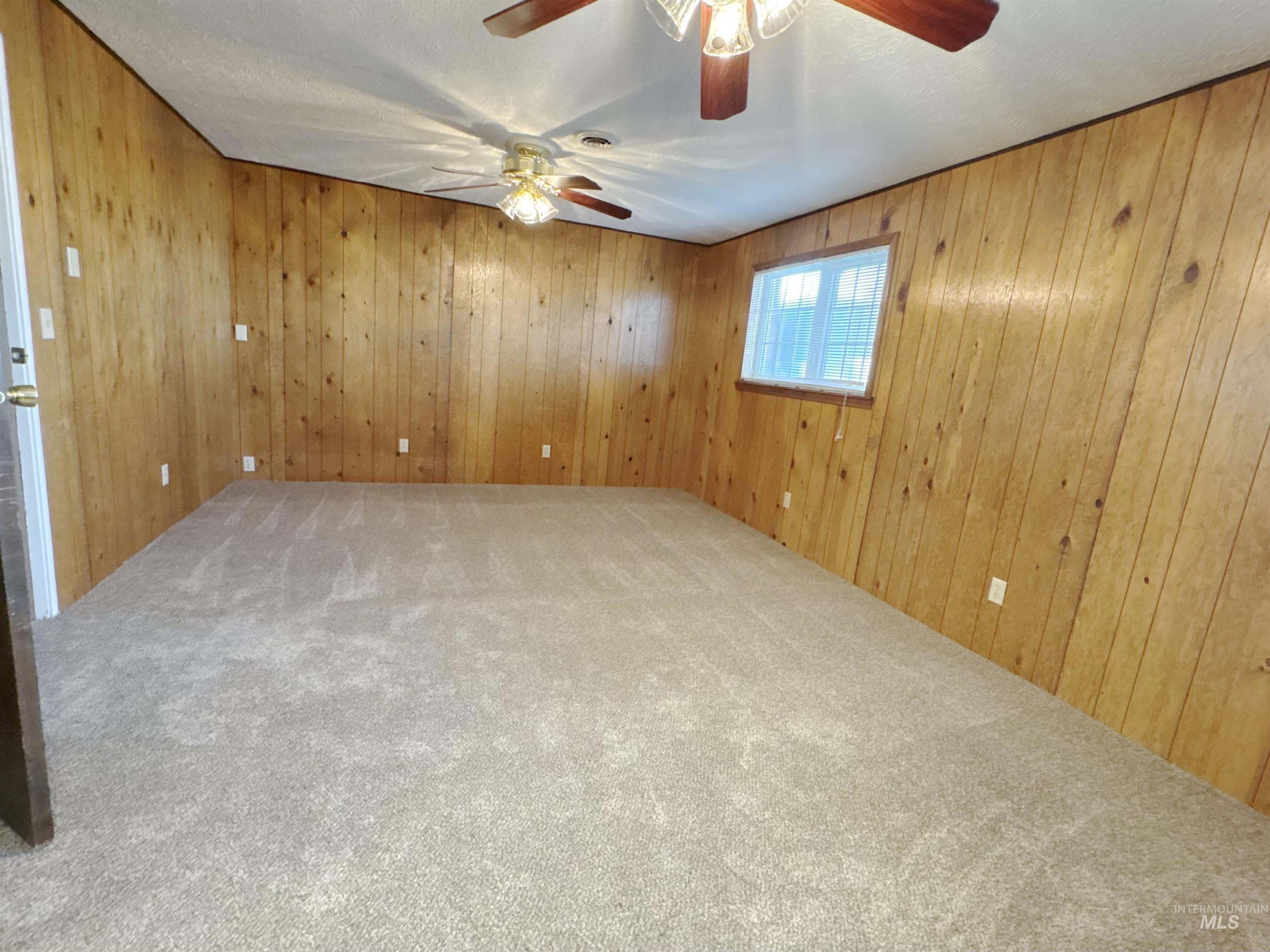 Carpeted empty room with wood walls and a ceiling fan