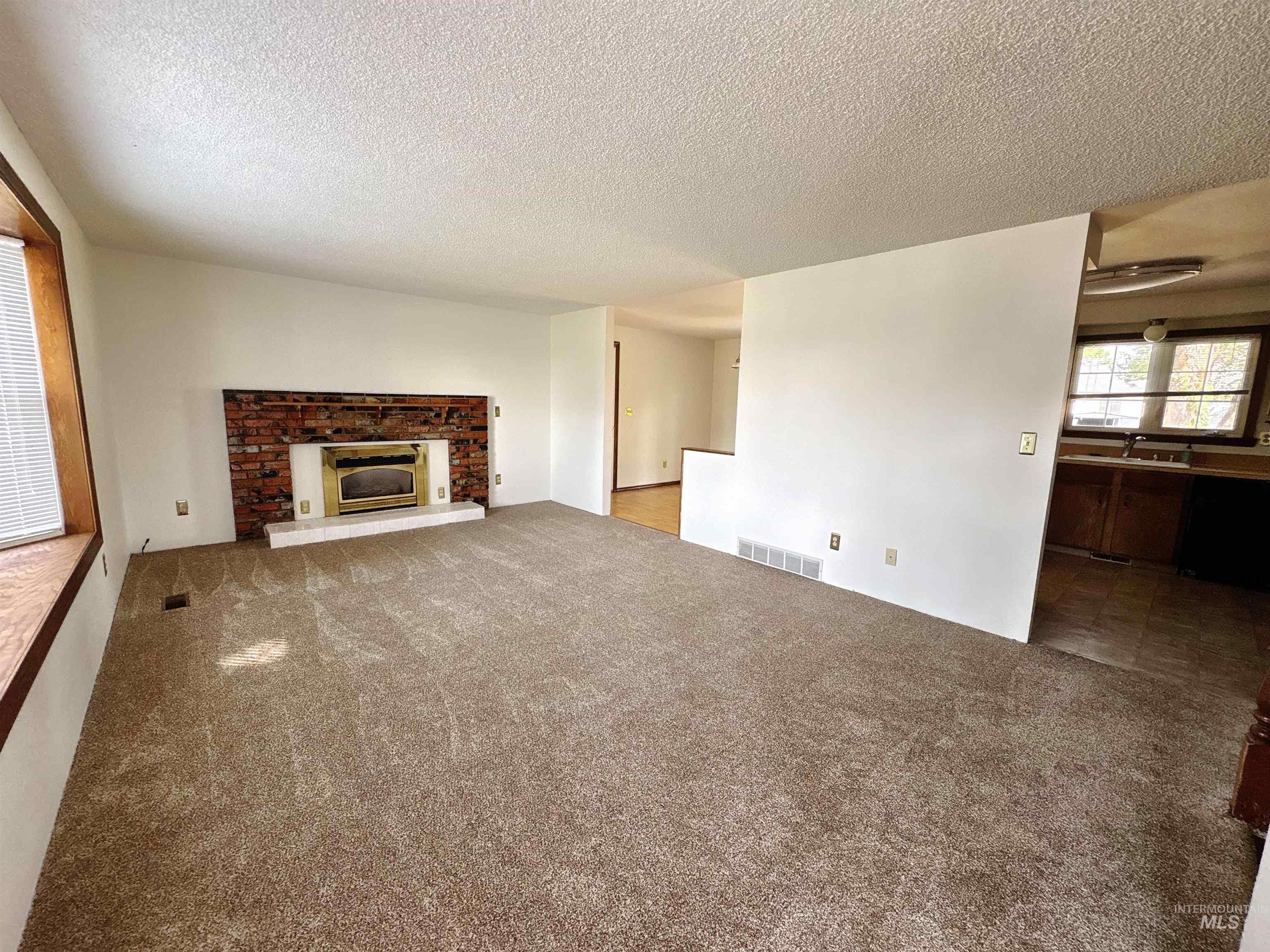 Unfurnished living room featuring carpet floors, a textured ceiling, and a fireplace