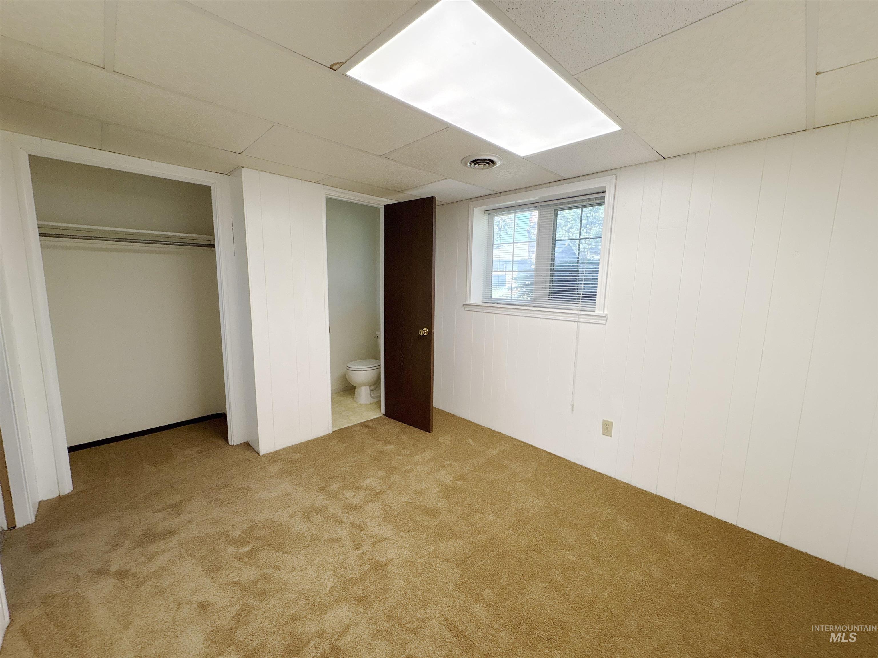 Unfurnished bedroom featuring carpet floors, ensuite bathroom, a closet, and wood walls