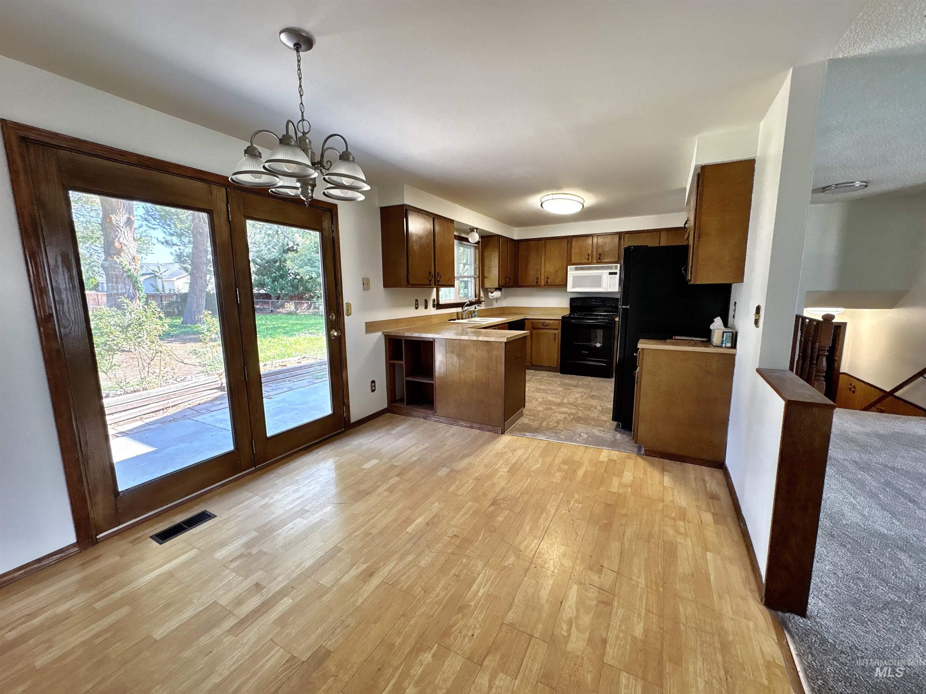 Kitchen featuring light countertops, a chandelier, a peninsula, black appliances, and hanging light fixtures