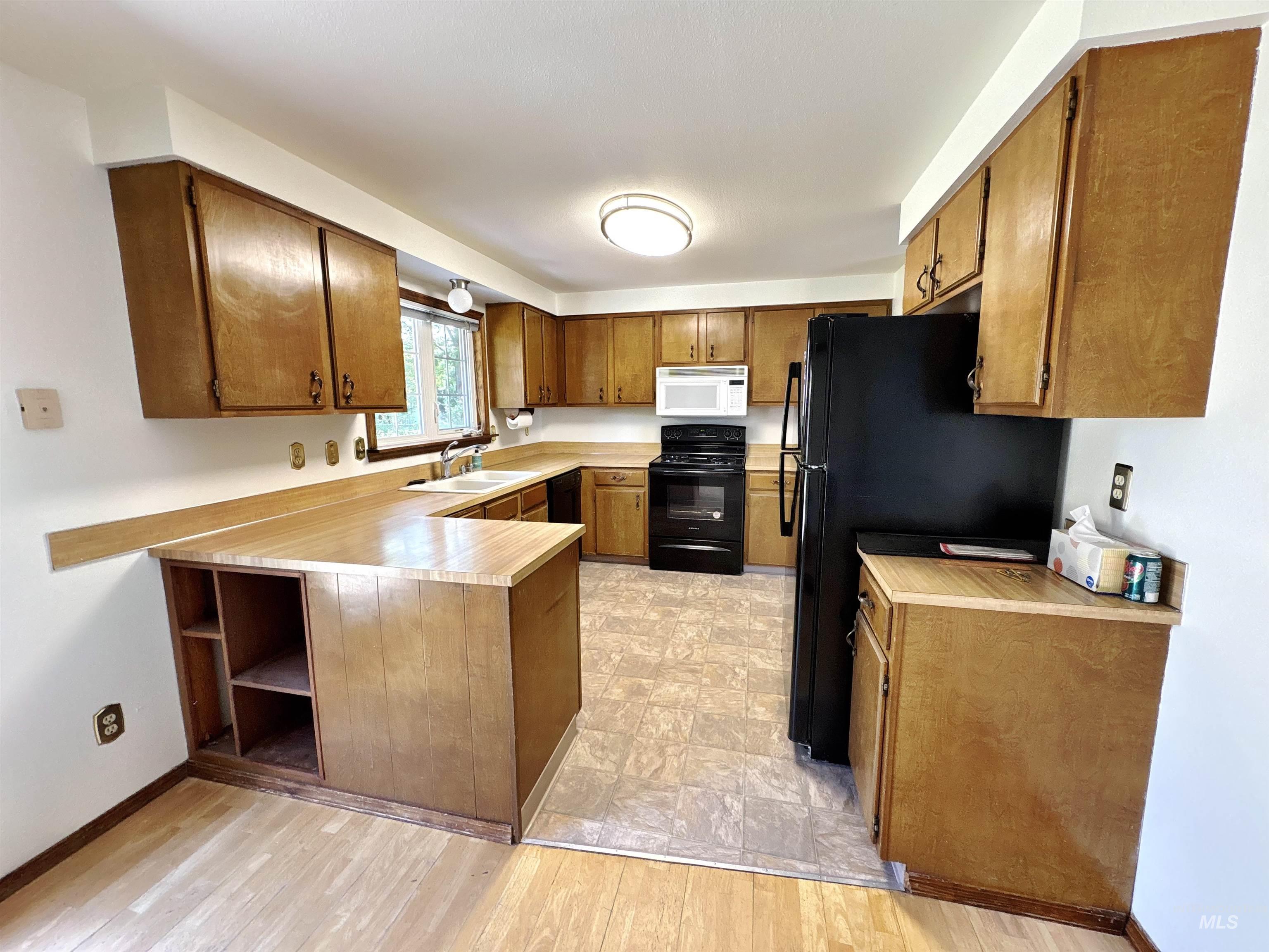 Kitchen featuring light countertops, brown cabinets, a peninsula, black appliances, and open shelves