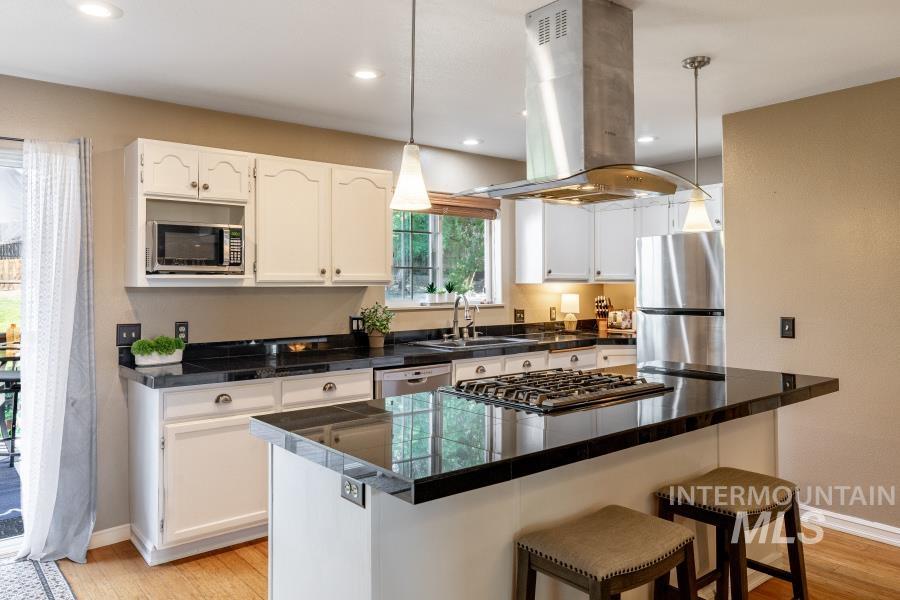 Kitchen featuring island range hood, light wood finished floors, a breakfast bar, decorative light fixtures, and recessed lighting