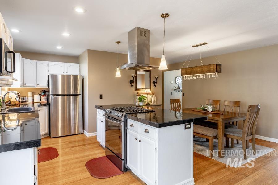 Kitchen with white cabinets, appliances with stainless steel finishes, island range hood, hanging light fixtures, and tile countertops