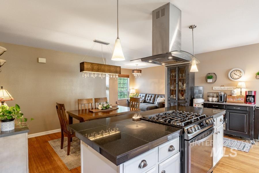 Kitchen featuring stainless steel gas range oven, hanging light fixtures, tile counters, island exhaust hood, and light wood-style floors