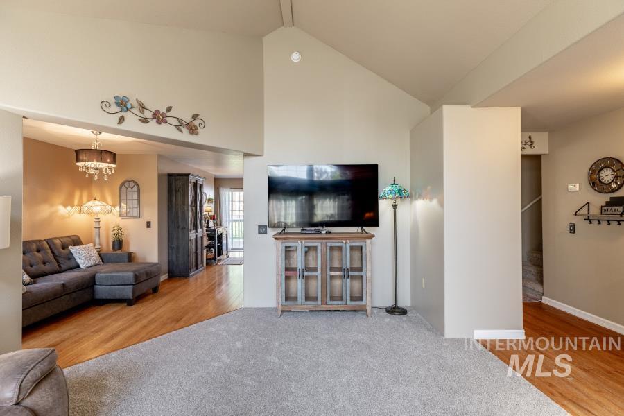 Living area with light wood-type flooring, high vaulted ceiling, light colored carpet, and a chandelier