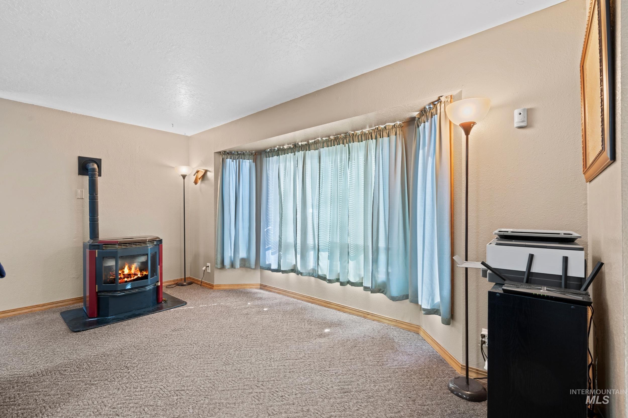Living area featuring a wood stove, carpet floors, and a textured ceiling